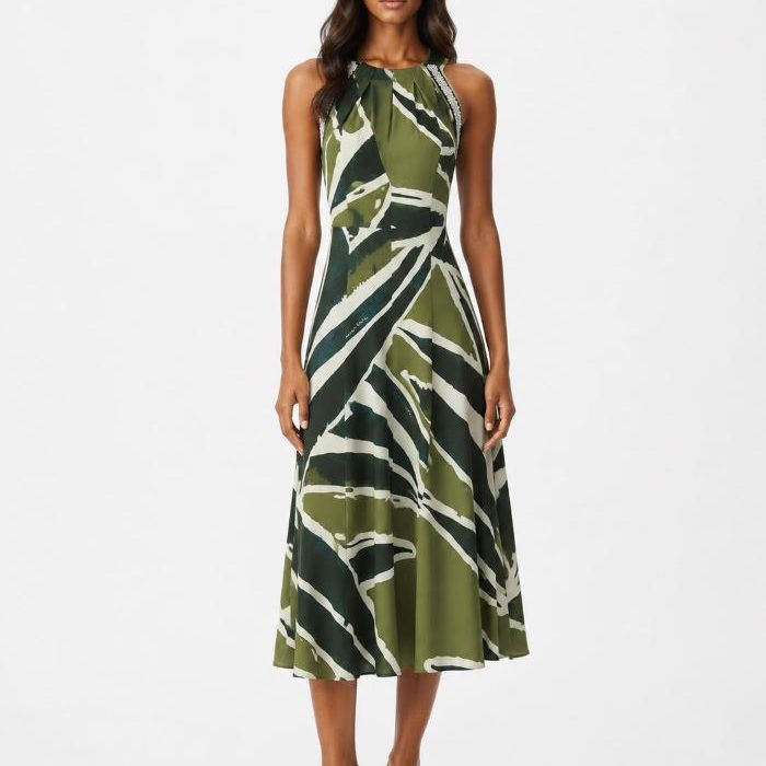 Modelo morena con vestido midi Grande de Malala en punto frío estampado verde, cuello halter con adornos en los tirantes y sandalias doradas sobre fondo blanco.